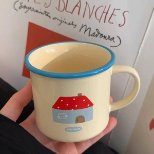 Ceramic Jolly House mug with blue rim and cartoon house illustration held by hand