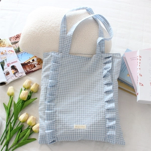 Détail d'un sac cabas en toile vichy bleu avec des volants et un logo sur fond de style de vie