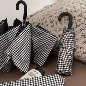 Close-up of black and white gingham sun umbrella with U-shaped matte handle and gold snap