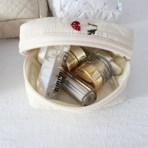 Detail of cream quilted cotton pouch with red mushroom embroidery showing interior storage