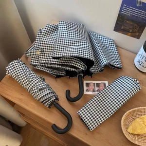 Detail of a folded black and white plaid umbrella with a matte hooked handle and storage bag