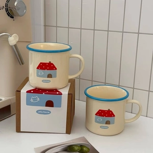 Close-up of ceramic mugs with blue rim, house illustration and gift box packaging