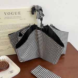 Classic black and white checkered foldable umbrella with matching storage bag on wooden desk