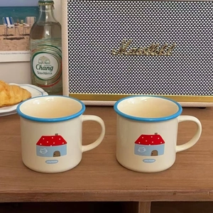 Detail of two cream ceramic mugs with blue rims and house patterns on a wooden table