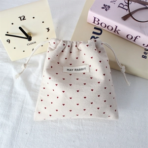 Close-up of beige drawstring pouch with red heart patterns and May Rabbit label