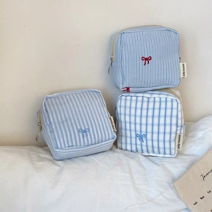 Macro detail of striped fabric makeup pouches with bow embroidery and zipper closure