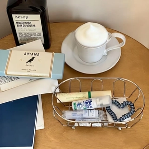 Minimalist silver wire mesh storage basket on wooden table with cosmetics and coffee