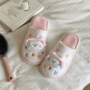 Détail de chaussons chat en peluche rose et blanc avec nœuds sur un drap douillet