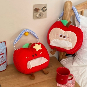 Plush apple tissue box cover with cute cartoon faces and handles in a cozy bedroom