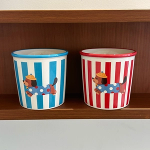 Detail view of striped ceramic puppy mugs in red and blue on a wooden shelf