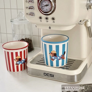 Ceramic striped dog mugs with cartoon dachshund patterns placed next to a vintage coffee machine