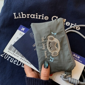 Gray nylon travel pouch with bear embroidery shown with passport and boarding pass