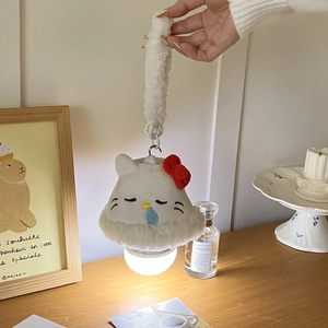 Detailed view of a white plush cat night light with warm glow and red bow on wooden desk