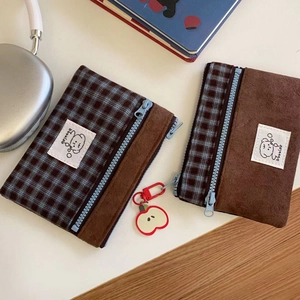 Detail of suede and plaid wallet with blue zipper and red apple charm attachment