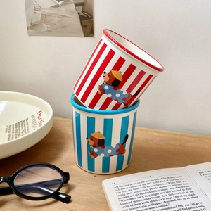 Striped ceramic puppy mugs in red and blue, shown in a cozy home setting on a wooden table