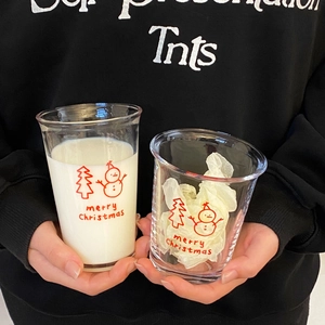 Close-up of hand holding a transparent glass cup with red snowman and Christmas tree patterns