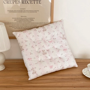 Floral quilted square chair cushion with rabbit and rose patterns in a cozy home setting