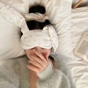 Detail of white rabbit ear sleep mask with pink Angel print on soft white bedding