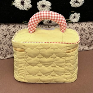 Dettaglio della trousse gialla trapuntata a cuori con manico a quadretti rossi e bianchi
