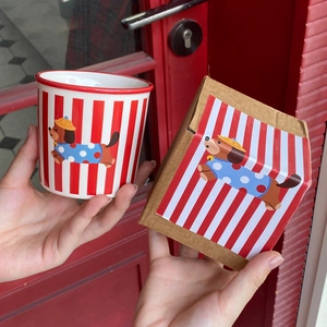 Close-up of ceramic striped puppy mug held by hands with its matching gift box packaging