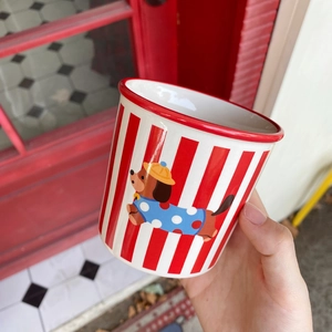 Person holding ceramic mug with red stripes and cute dachshund puppy illustration