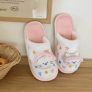 Gros plan de chaussons chat avec casque rose et broderie peluche sur sol en bois