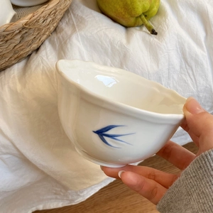 Dettaglio di ciotola in ceramica bianca con bordo ondulato e motivo di rondine blu