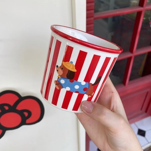 Close-up of hand holding a red and white striped ceramic mug with a cute puppy illustration