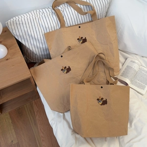 Close-up of three brown kraft paper tote bags with cartoon dog embroidery on white bed
