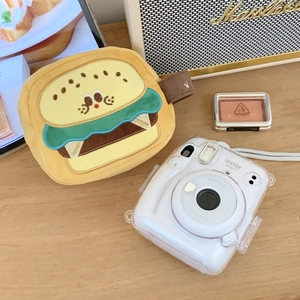 Plush burger-shaped camera bag detail with handle on wooden table near polaroid