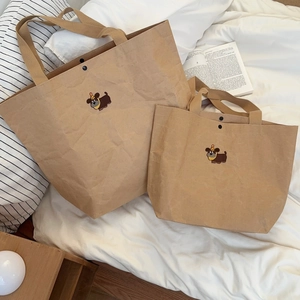 Brown kraft tote bag with embroidered cartoon dog and strap handles on white bedding