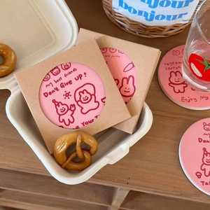 Close-up of pink ceramic rabbit coasters with cartoon illustrations in paper packaging