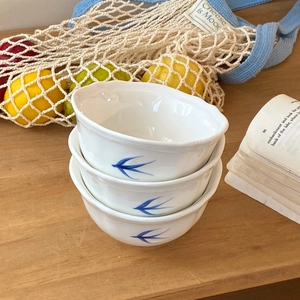 Tre ciotole in ceramica bianca con motivi a rondine blu e bordo ondulato su tavolo legno
