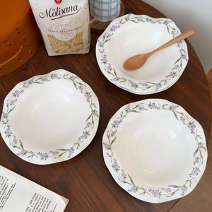 Close-up of wavy ceramic plates with purple lavender floral pattern on dark wood table