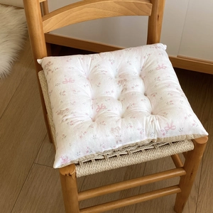 Detailed view of square floral cushion with quilting on a wooden chair in a cozy room