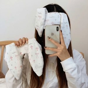 Close-up of white plush bunny ear headband with pink bows and angel print patterns