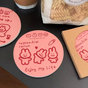 Pink silicone coaster with cartoon rabbit and pig pattern next to packaging box