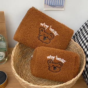 Close-up of embroidered bear faces on soft brown plush makeup bags in a woven basket