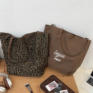 Detail of leopard print tote and coffee brown canvas bag with 'merci' text on table