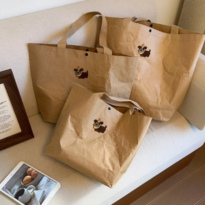 Three sizes of kraft paper tote bags with cartoon dog embroidery on a beige sofa