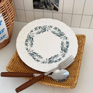 Detail of floral ceramic plate with embossed edge on straw mat with wooden cutlery