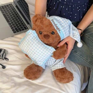 Detail of plush brown teddy bear in blue plaid pajamas with a matching sleeping hat