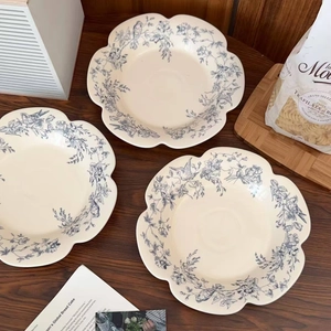 Detail of scalloped ceramic plate with blue vintage floral and bird pattern on dark wood