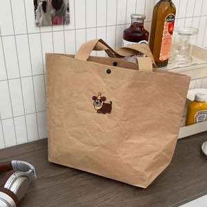 Detail of cartoon dog embroidery on a crinkled kraft paper tote bag with snap closure