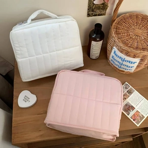 Vertical quilted cosmetic bags in white and pink displayed on a wooden surface