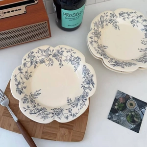 Detail of scalloped ceramic plate with blue floral and bird patterns in a rustic setting