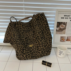 Detail of leopard print canvas tote bag featuring an oval handmade metal logo tag