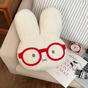 Close-up of cute cream plush rabbit hot water bottle with red glasses on a sofa