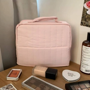 Detailed view of pink quilted makeup bag with handle on a wooden dressing table