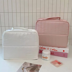 Detailed view of quilted makeup bags in pink and white with handle and vertical texture